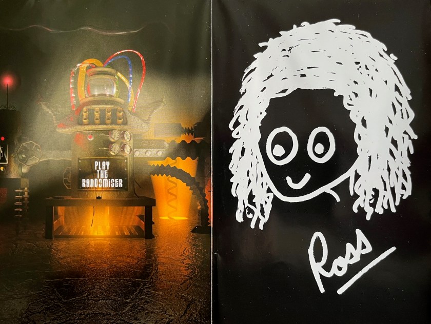 Double-page spread from the booklet with Ross Noble's Randomist DVD. The left page shows a large mechanical machine with dials and pipes, with text lit up on a central panel that says Play The Randomiser. The right page shows a crude child-like drawing of a smiling face with a lot of straggly hair, below which is a signature that says Ross with a line underneath it.