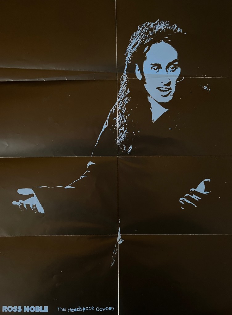 A fold-out poster from Ross Noble's Headspace Cowboy DVD, showing an image of him talking on stage that's been filtered to be blue in colour wherever the light falls on his face, hands, clothing and hair, while the rest of him is black to match the background.