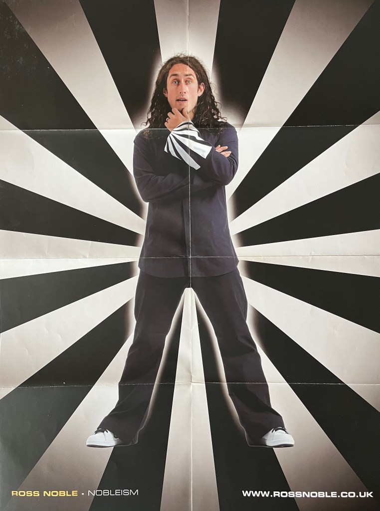 A poster of Ross Noble standing in front of a back and white striped spiral background. The same black and white stripes are on the large cuff of his navy shirt, as he strokes his chin thoughtfully. He's also wearing black trousers and white trainers. The poster was issued with his Nobleism DVD.