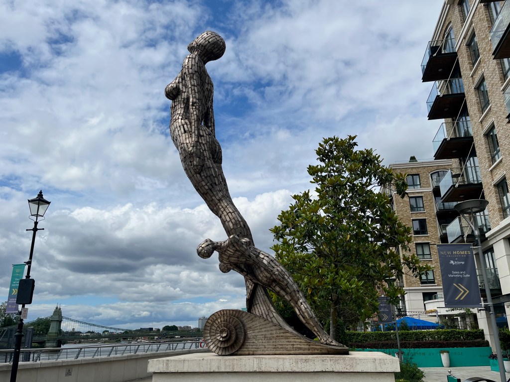 Figurehead statue by John Kirby, viewed from the left side. Symbolising the figurehead of a ship, a large female figure leans forward, while two smaller figures are at her feet standing on a shell-like base.