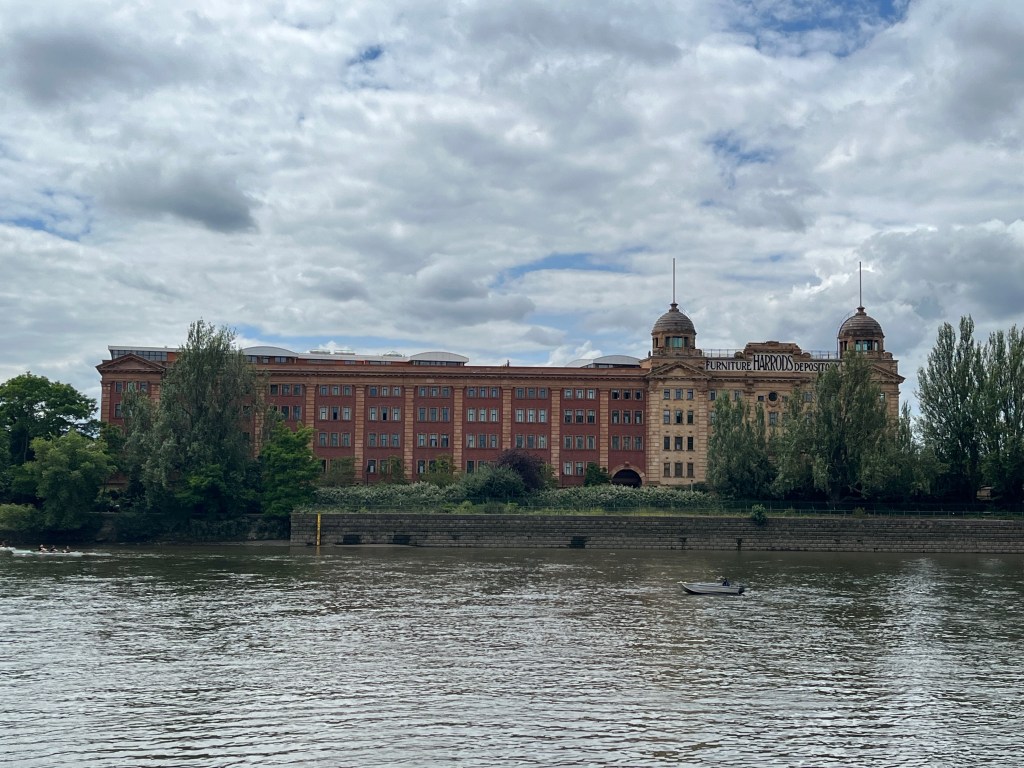The historic Harrods Furniture Depository, a long 4 story building by the Thames. On the right end are two additional rooms under domes on the roof, either side of the Harrods Furniture Depository sign.