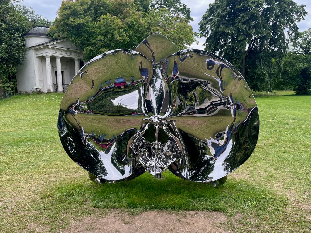 A large sculpture representing an orchid in bloom, with 3 large round leaves that are open to reveal its centre. The surfaces of the meta sculpture are curved in various ways and are very reflective.