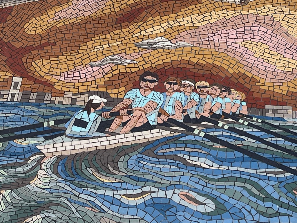 Close-up of the Cambridge team of rowers in the Oxford and Cambridge Boat Race mural, wearing light blue shirts.