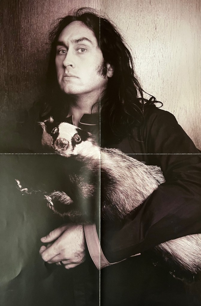 Poster from Ross Noble's Mindblender DVD, showing a black and white photo of Ross holding a badger. Ross has a serious expression and the badger looks a bit startled, as if Ross didn't expect to be photographed carrying it away.