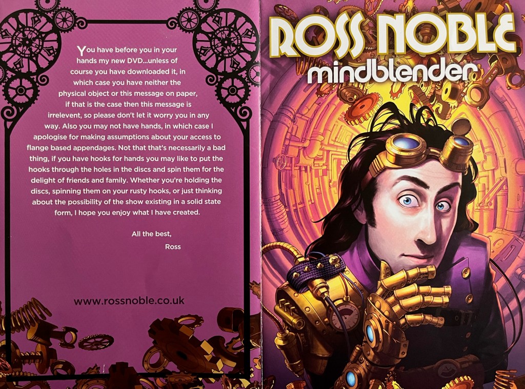 Double-page spread from the cover of the booklet with Ross Noble's Mindblender DVD. The front cover on the right shows an image of Ross looking thoughtful with a gold robotic arm. The page on the has a message from Ross. You have before you in your hands my new DVD, unless of course you have downloaded it, in which case you have neither the physical object or this message on paper. If that is the case then this message is irrelevant, so please don't let it worry you in any way. Also you may not have hands, in which case I apologise for making assumptions about your access to flange based appendages. Not that that's necessarily a bad thing, if you have hooks for hands you may like to put the hooks through the holes in the discs and spin them for the delight of friends and family. Whether you're holding the discs, spinning them on your rusty hooks, or just thinking about the possibility of the show existing in a solid state form, I hope you enjoy what I have created. All the best, Ross.
