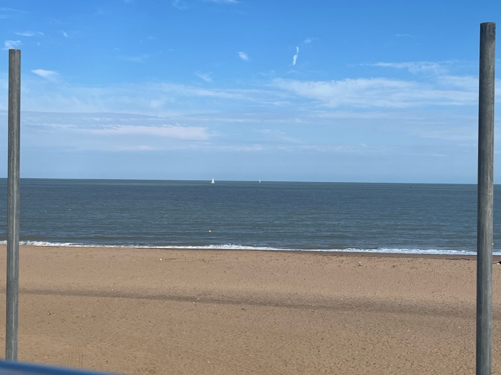 The golden sands of Ramsgate Beach. A boat with white sails is visible out in the sea.