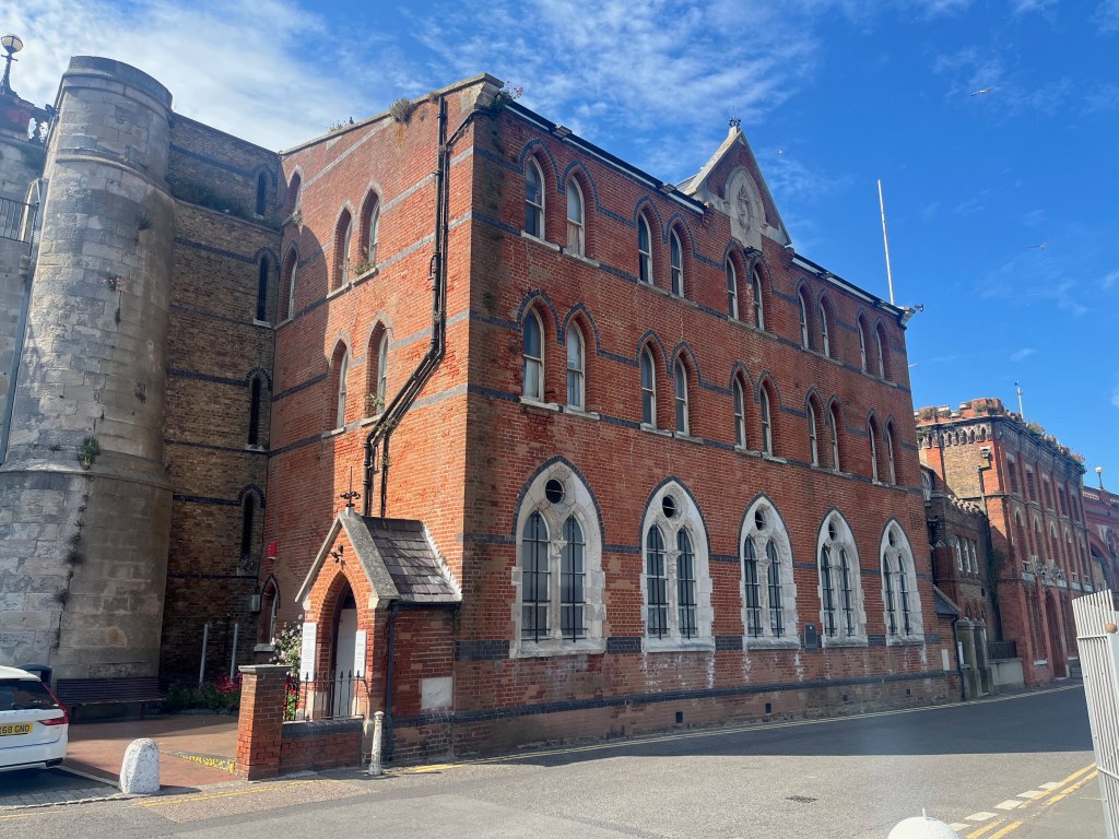 A large three-storey building called the Sailors Church in Ramsgate, with 5 large arched windows on the ground floor, and 5 pairs of smaller arched windows on each of the upper two floors. The roof is flat apart from a small triangular section in the centre. A triangular roofed porch sticks out from the left wall as the entrance to the building.