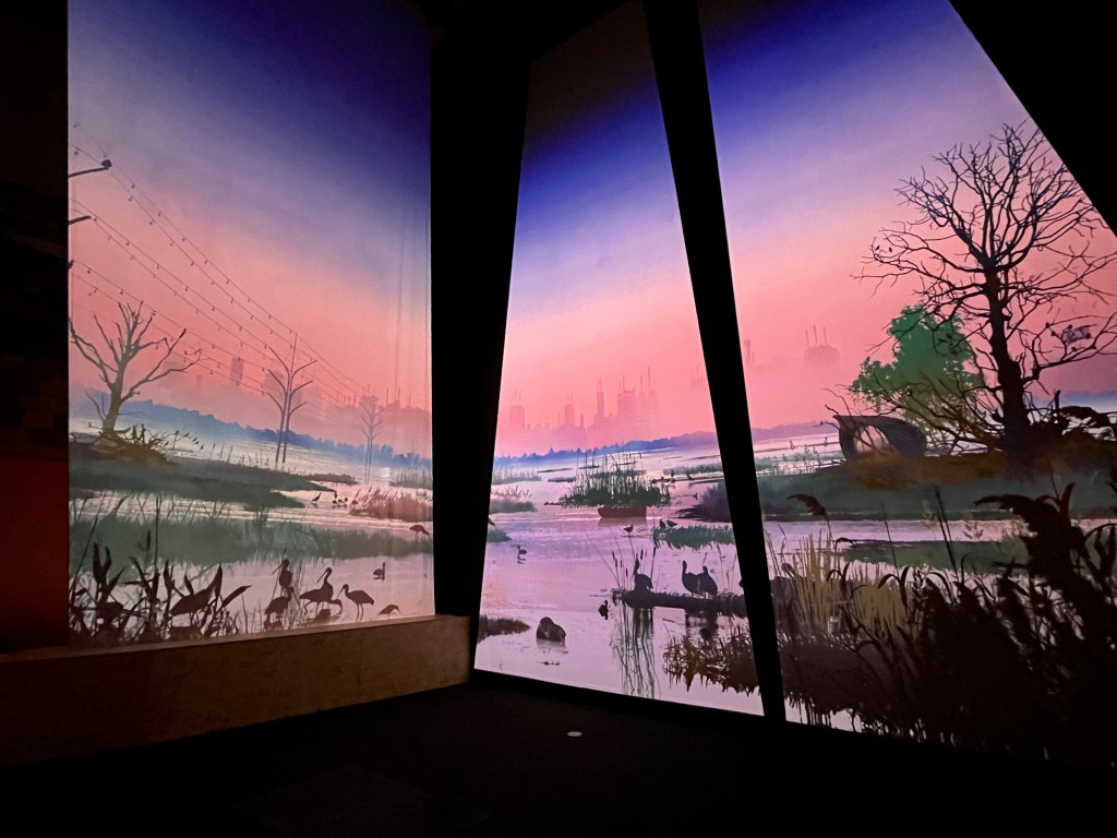 A large floor to ceiling animated display spanning two walls around a corner, showing lots of birds inhabiting a landscape of water with patches of greenery scattered throughout.