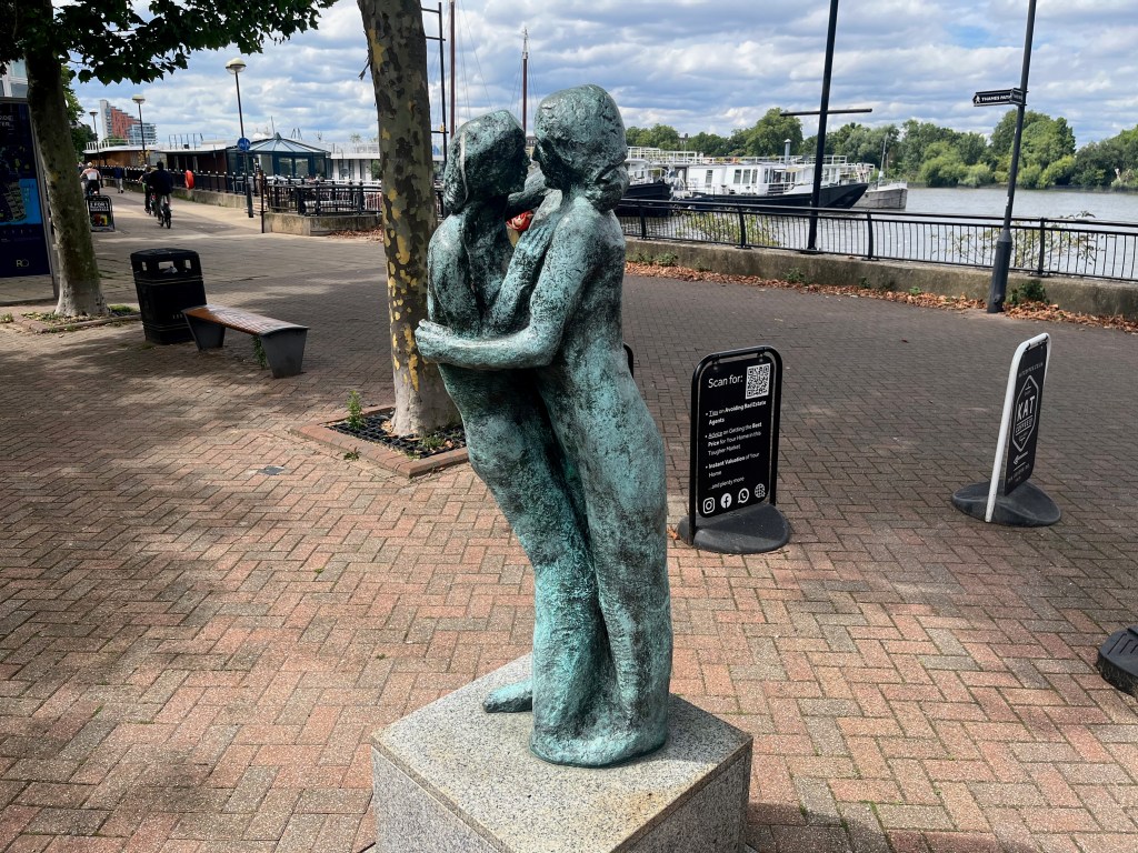 Sculpture of two people standing and embracing, their heads close as if about to kiss.