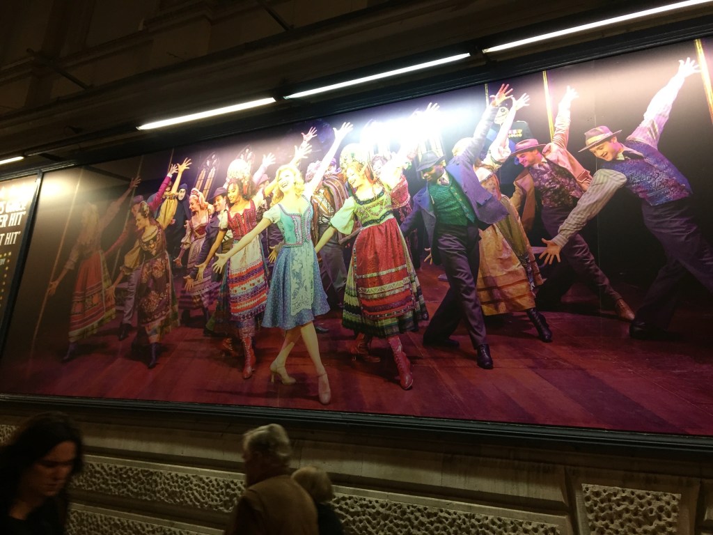Poster on the Garrick Theatre showing a long line of people in colourful costumes dancing in the musical Young Frankenstein.