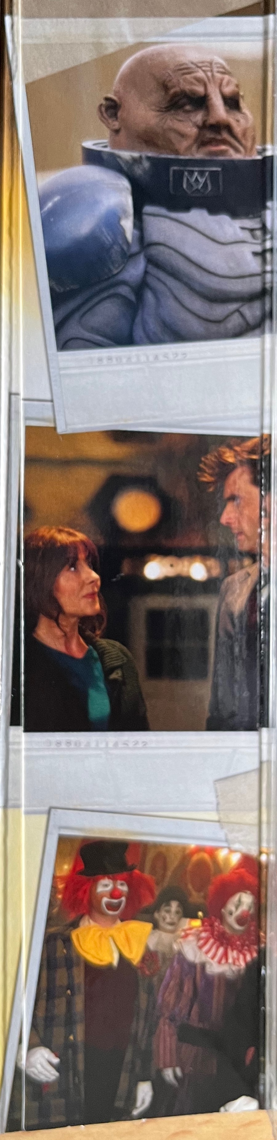 A vertical strip of 3 polaroid style photos shown within the DVD box set of The Sarah Jane Adventures, showing images from the series. The top one shows a Sontaran warrior, the middle one shows Sarah Jane with David Tennant as the 10th Doctor in his Tardis, and the third shows three people dressed as clowns.