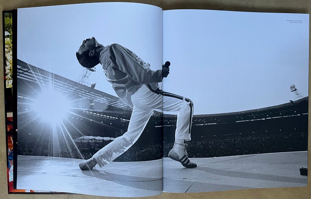 Double-page spread from the book for the Freddie Mercury exhibition at Sotheby's, showing Freddie on stage at Wembley from behind, as he leans back with his legs astride.