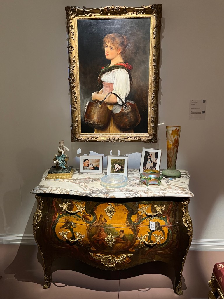 A painting of
a young Venetian woman with two copper kettles resting on her arm, above a French commode desk on which are photos of Freddie and his cats.