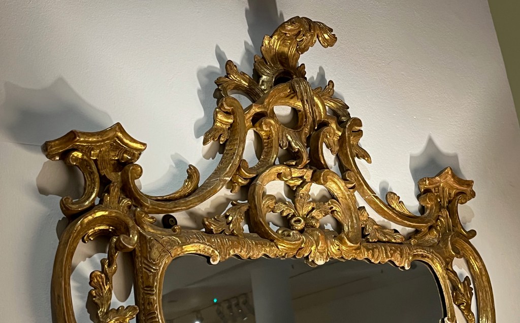 Close-up of the top of the ornate frame surrounding a George III mirror.