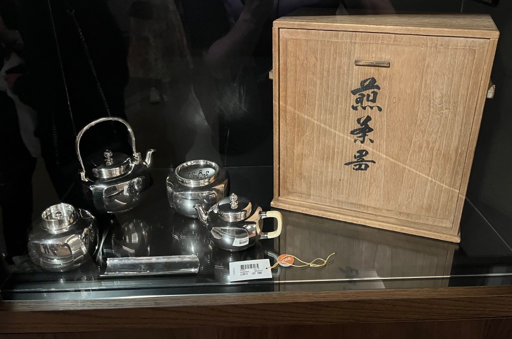 A Japanese silver tea set with a ewer for hot water, a ewer for pouring with ivory handle, an incense burner, a tea caddy and a tea scoop. The set is accompanied by a wooden storage box, with Japanese writing in black down the centre.