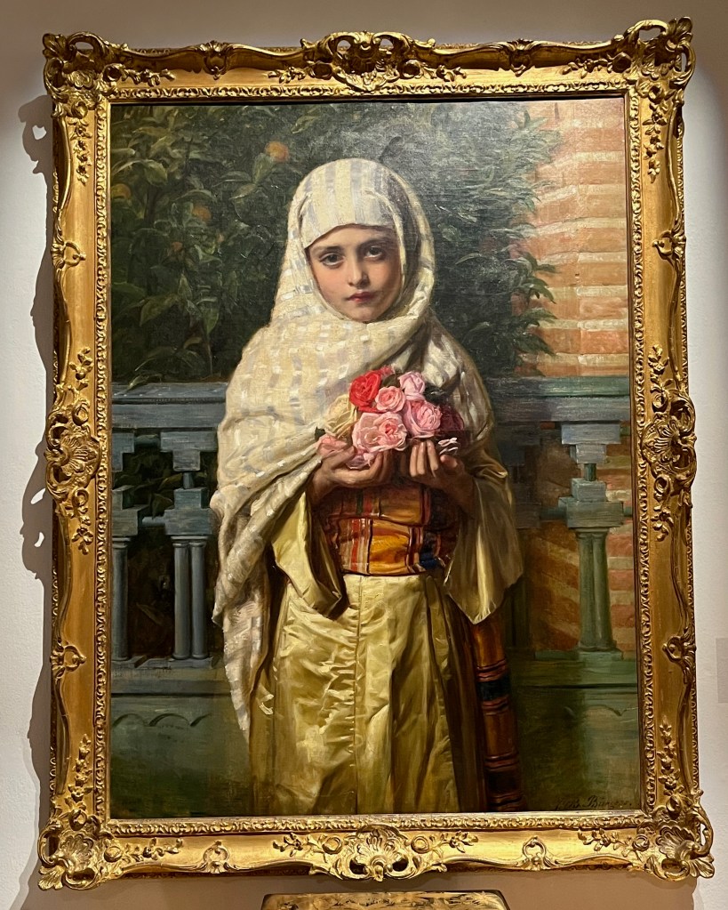 Oil on canvas painting by John Bagnold Burgess called A Spanish Girl. The girl in question is wearing a white shawl around her head, with shining silvery going down it, over a golden yellow robe. She's holding a small bunch of flowers, most of which are pink, but there's also a red one and a yellow one.