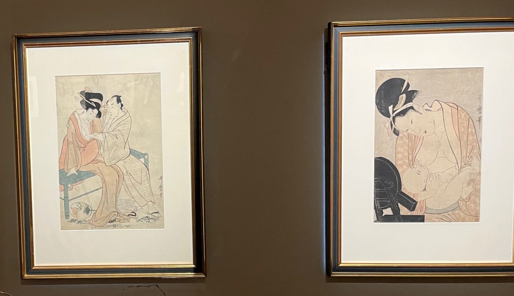 Two Japanese woodblock prints by Kitagawa Utamaro. The first shows a couple sitting on a bamboo bench. The woman has her hand on the man's arm as he reaches inside her open robe to touch her right breast. In the other picture, A mother tenderly nurses her child while sitting in front of a small black lacquered mirror on a stand. Their eyes appear to meet in familial affection as the healthy infant suckles among the falling pleats of his mother’s open robes.