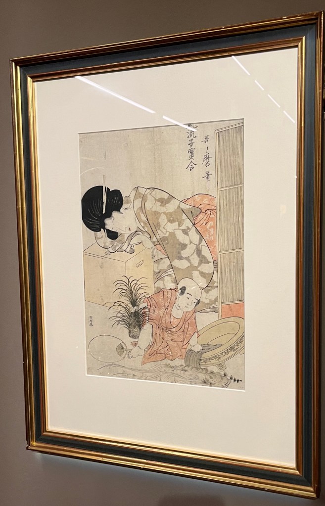 Japanese woodblock print by Kitagawa Utamaro called Goldfish. A mother has fallen asleep, her head resting on a box. Meanwhile her young son has uprooted a plant from a goldfish bowl and has tipped up the bowl causing water and fish to cascade over the floor.