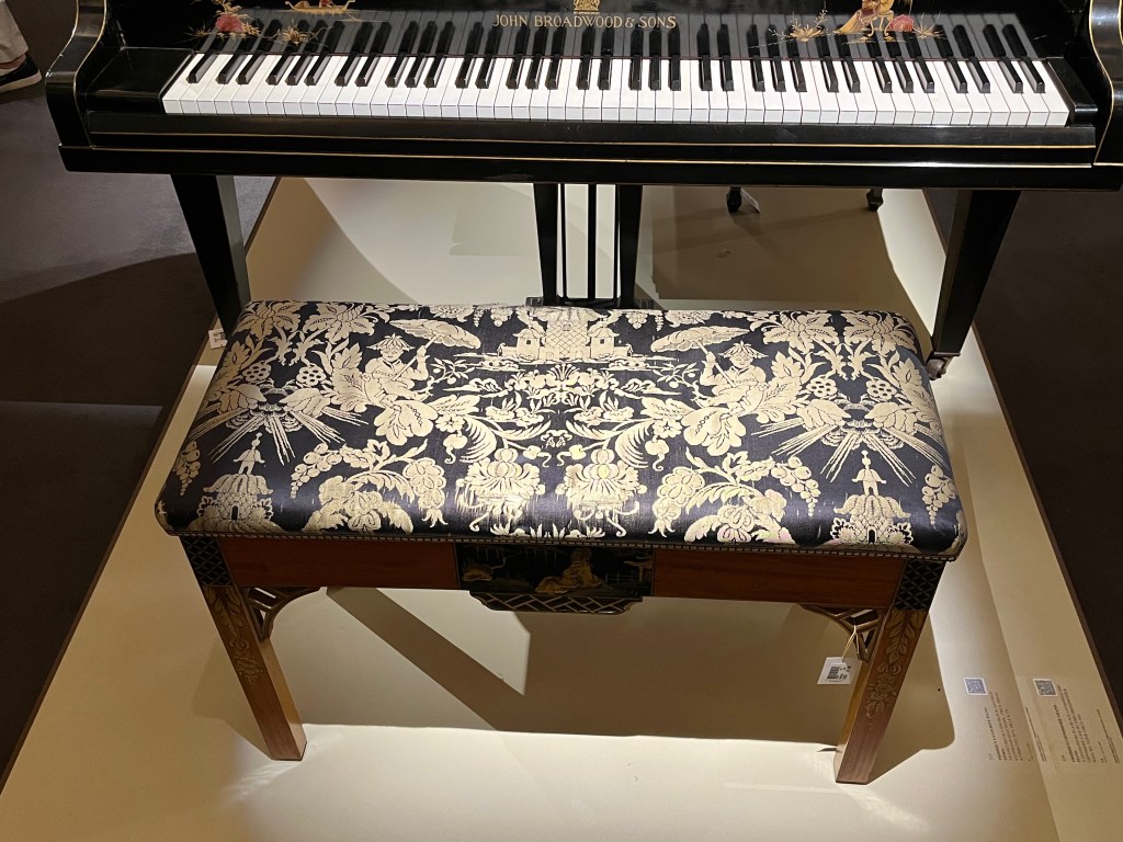 A piano stool with the black seat cover decorated with a pattern of gold flowers and foliage.