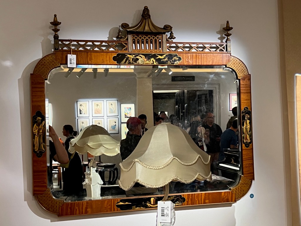 A large rectangular mirror with curved corners on the wooden frame, with artwork of figures in the middle of each side of the frame, and a stylised pagoda above on the top.
