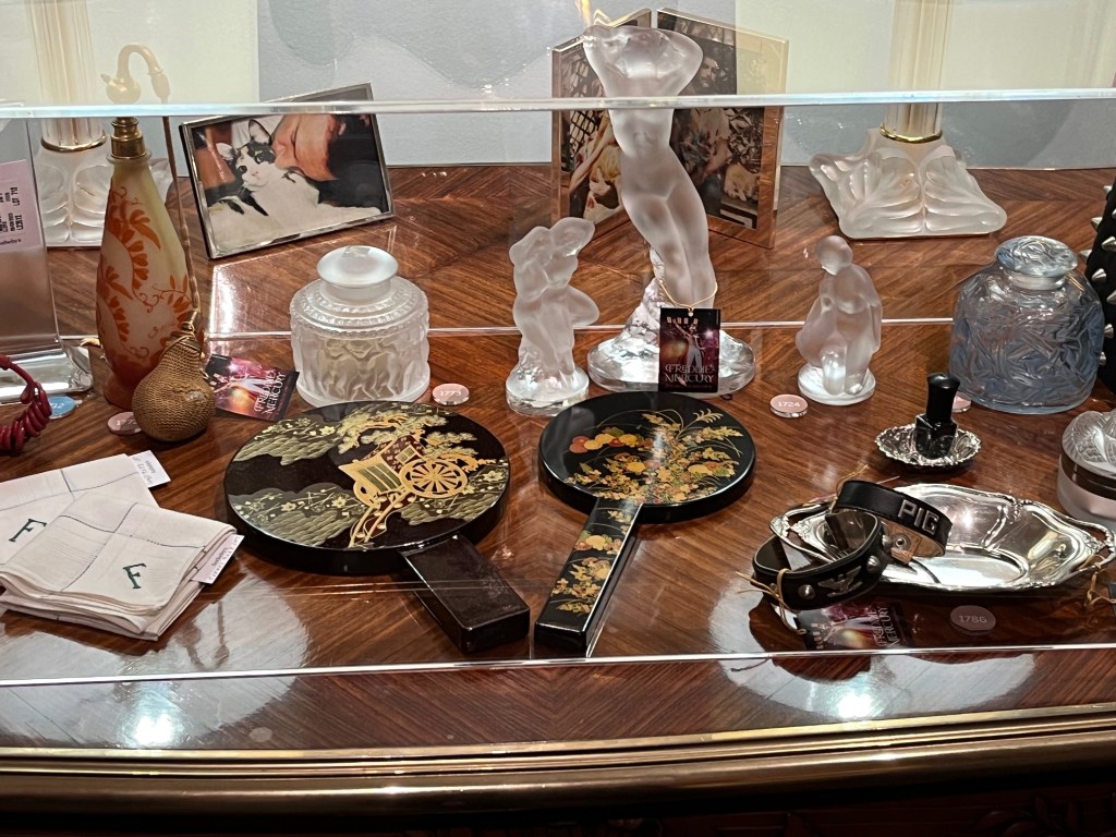 Various objects in a glass case on a table, including a couple of ornately decorated paddles, small statues, and a small black collar with the word Pig on it.