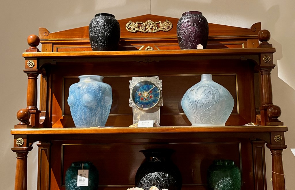 Ornately sculptured vases by René Lalique and a mantel clock with a blue clock face on a carved silver block.