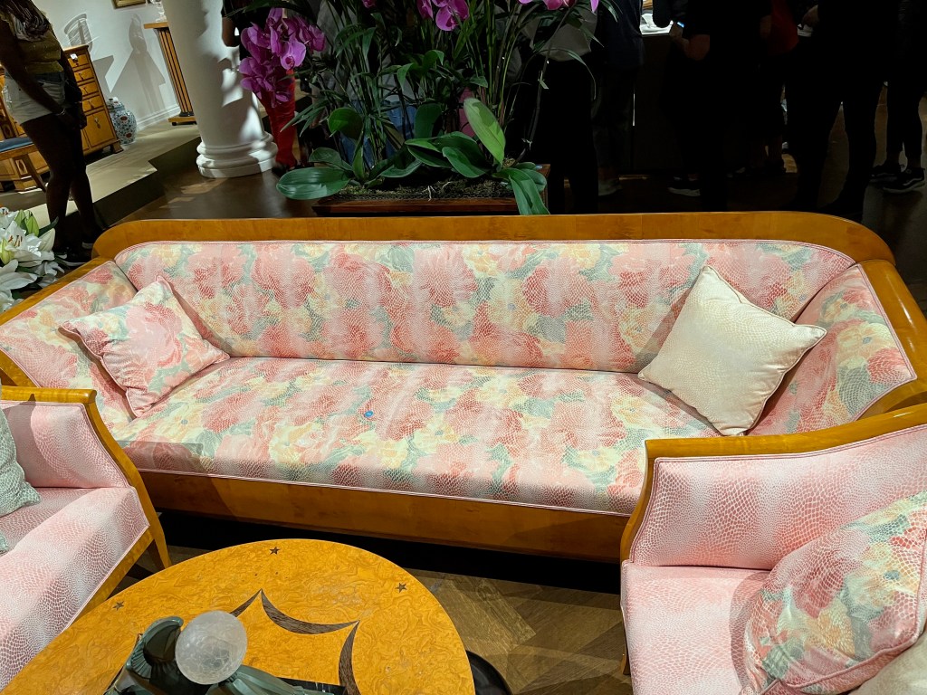 A 3-seater sofa covered in a pink silk fabric with a snakeskin style floral pattern.