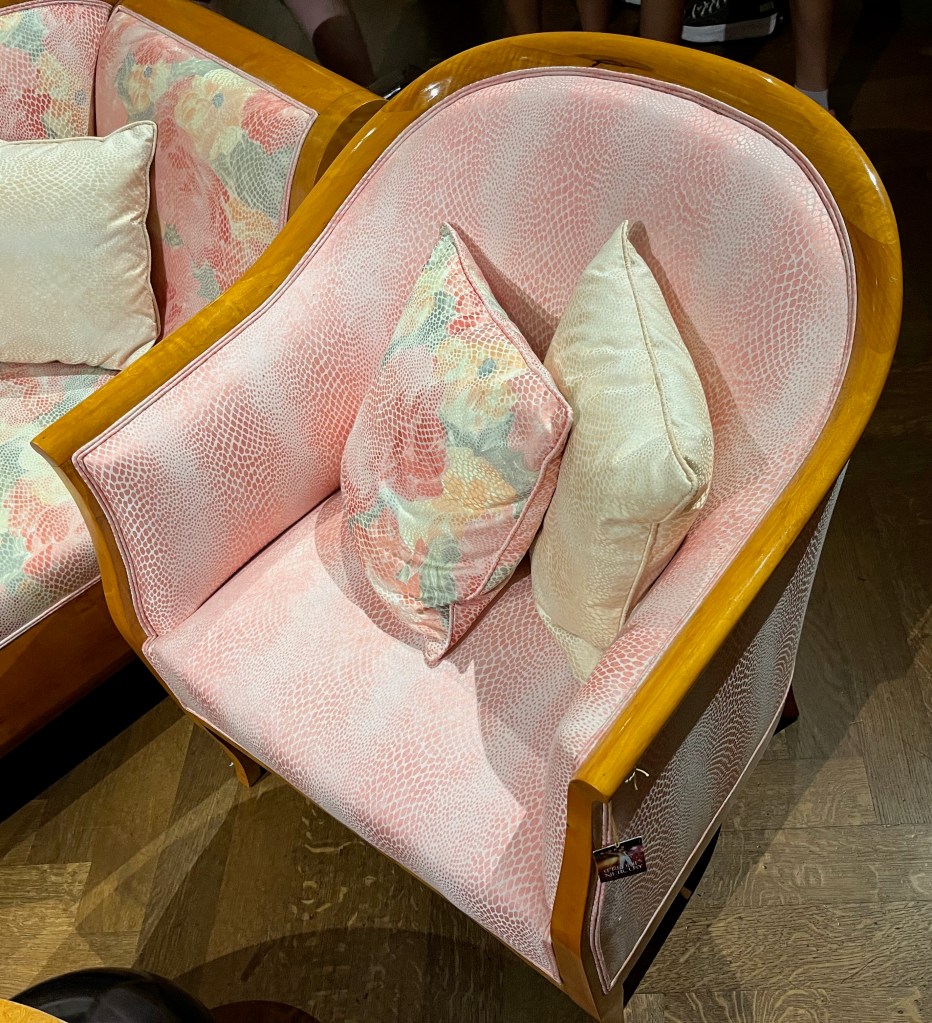 A tub style armchair with a rounded back, covered in a pink silk fabric with a snakeskin style floral pattern.