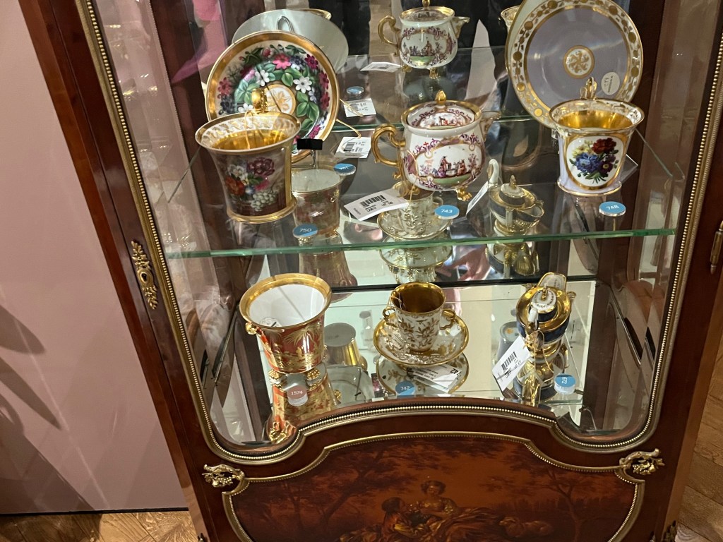 Colourful crockery and statues on glass shelves inside a French gilt-bronze mounted mahogany and vernis martin display cabinet.