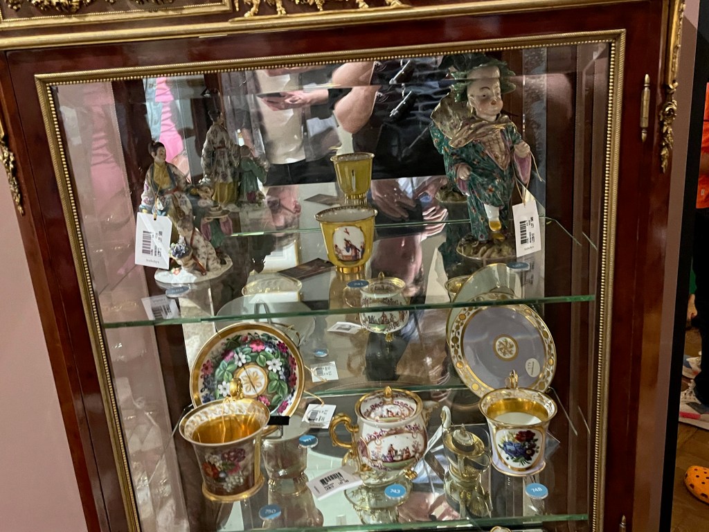 Colourful crockery and statues on glass shelves inside a French gilt-bronze mounted mahogany and vernis martin display cabinet.