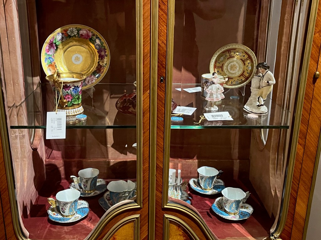 Items of crockery in various colourful designs, plus a couple of small statues, inside a display case.