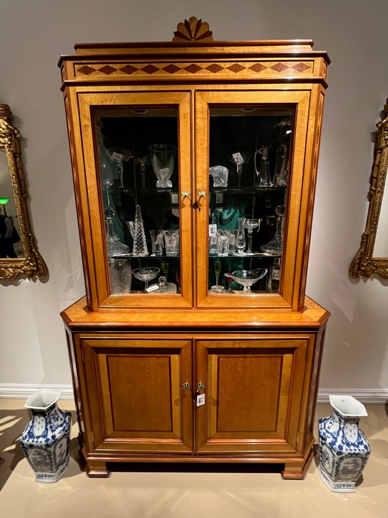 Maple and mahogany display cabinet designed by Robin Moore Ede, with two glazed panel doors, behind which are two glass shelves filled with glassware. There is also a cupboard at the bottom of the cabinet.