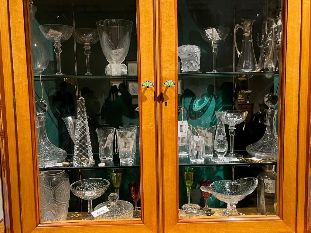 A selection of ornate glassware seen through the glazed doors of a maple and mahogany display cabinet.