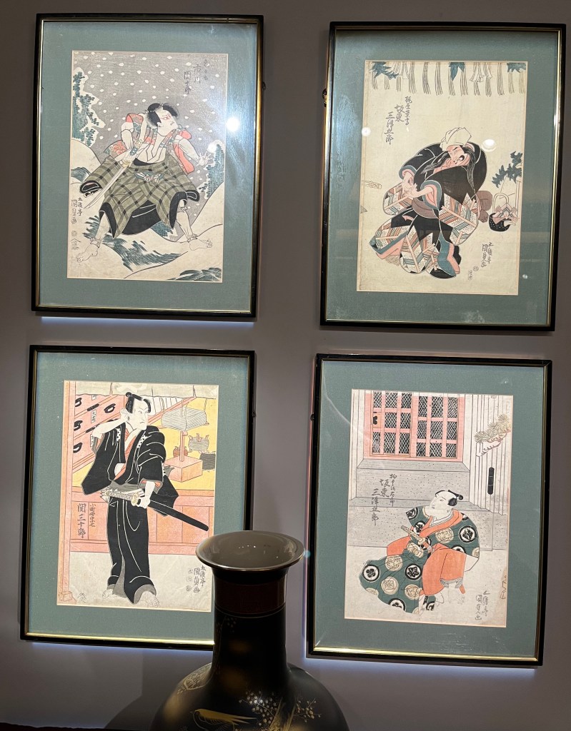 Four Japanese woodblock prints by Utagawa Kunisada showing actors in various outfits and poses, including one in the snow and one wearing a black robe while holding a sheathed sword,