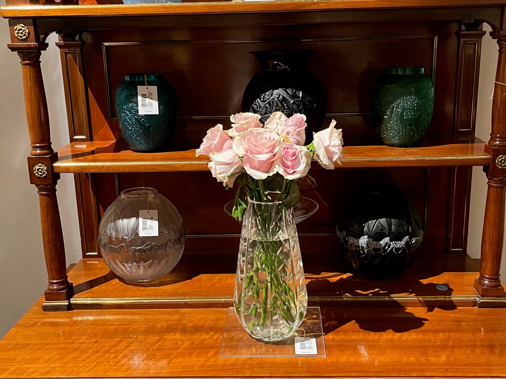Ornately sculptured vases by René Lalique, one of which is black with a design of zebras around its centre, while another is clear and holding a bunch of pink flowers.