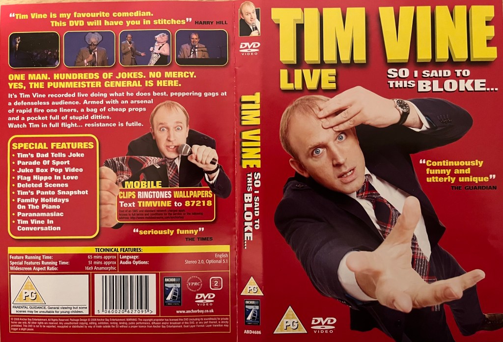 DVD cover spread for Tim Vine, So I Said To This Bloke. The front shows him placing a few fingers to his forehead with a worried expression on his face, as he reaches out towards us with his other hand, while the back cover shows him talking as he holds a microphone with one hand, while holding out part of his tie with the other, along with a few photos from the show.