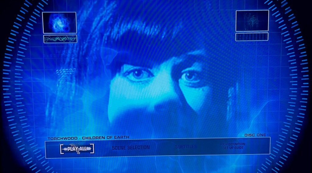 Blu-ray menu for Torchwood, Children Of Earth, showing a blue-tinted image of Gwen Cooper's face in close-up, with the lower half in shadow. The options along the bottom are Play All, Scene Selection, Subtitles and High Definition Set Up Guide.