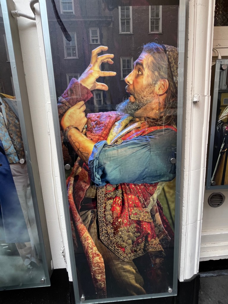 A poster of Fagin in the Oliver musical, grappling with his right arm, as his right hand is reaching for his face as if about to grab it tightly.