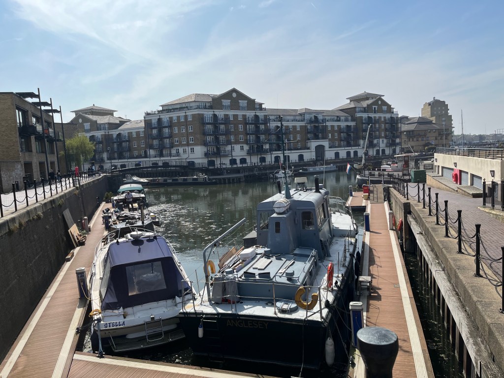 Two boats moored in Limehouse Basin, looking out into a larger dock area with 5 and 6 storey buildings on the far side.