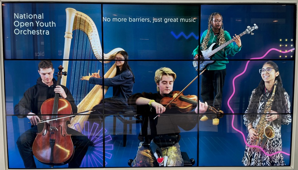 A poster image of the National Open Youth Orchestra, spread across a three by three grid of screens. Alongside the name of the orchestra at the top it says No more barriers, just great music. The image shows five members of the orchestra performing on a cello, harp, violin, bass guitar and saxophone.