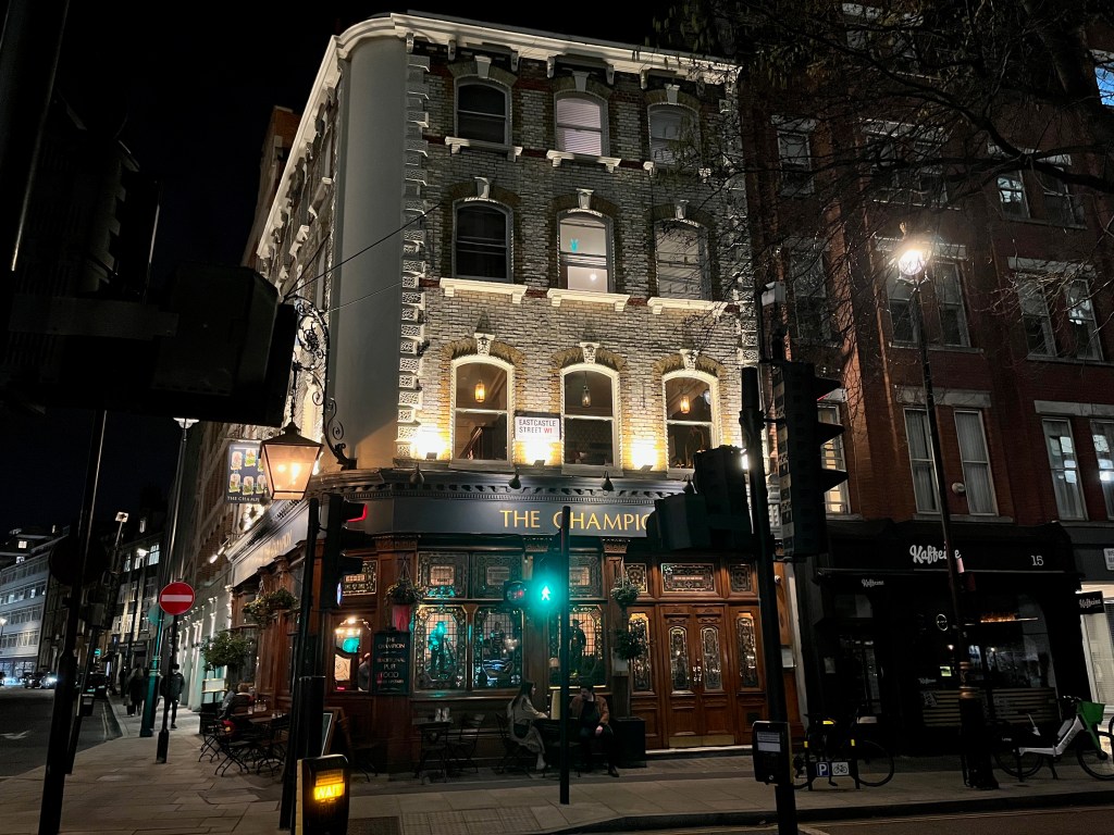 The Champion pub, a 4-storey building on a street corner, lit up at night.