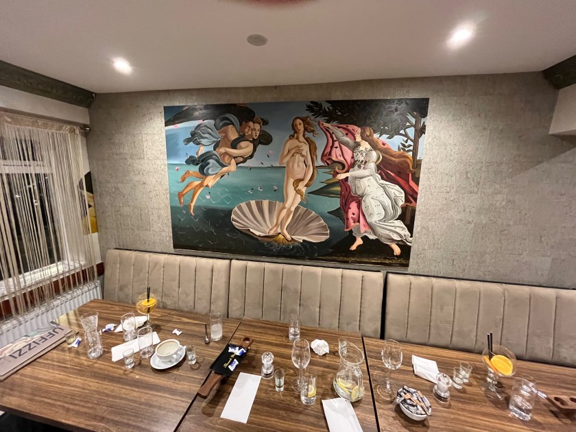 Long table setting at the Uffizzi restaurant, with various empty glasses from the group that had been sitting there. On the wall behind the table is The Birth of Venus painting by Botticelli 