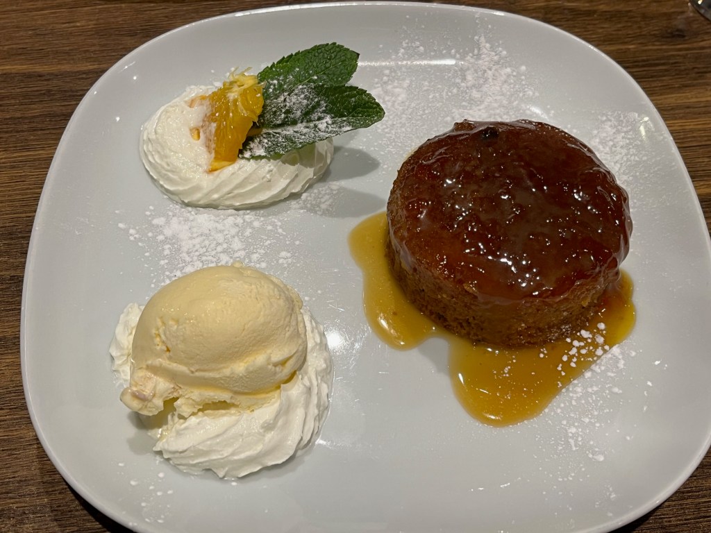 Sticky toffee sponge pudding with a scoop of vanilla ice cream.