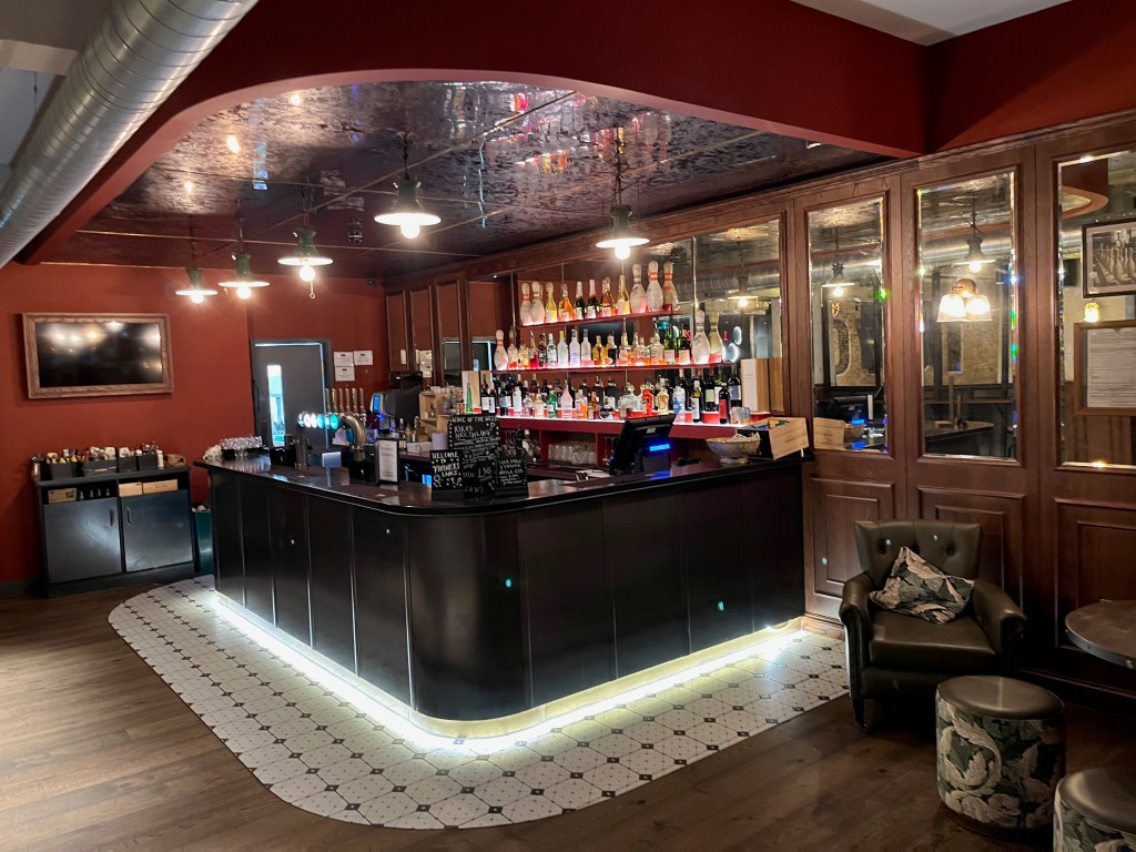 The bar area at Vintners Lanes, with 3 shelves filled with bottles at the back.