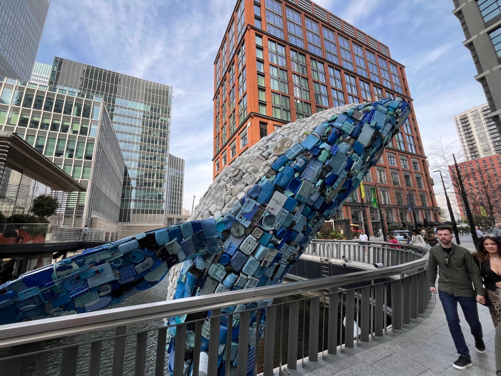A side view of the 4-storey high blue whale sculpture made out of plastic litter in Canary Wharf, where you can see one of its fins outstretched.