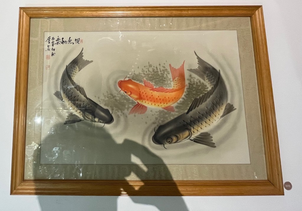 A painting of 3 carp swimming around, the middle one being orange in colour while the other two have black skin on the top and whiter skin on their undersides.