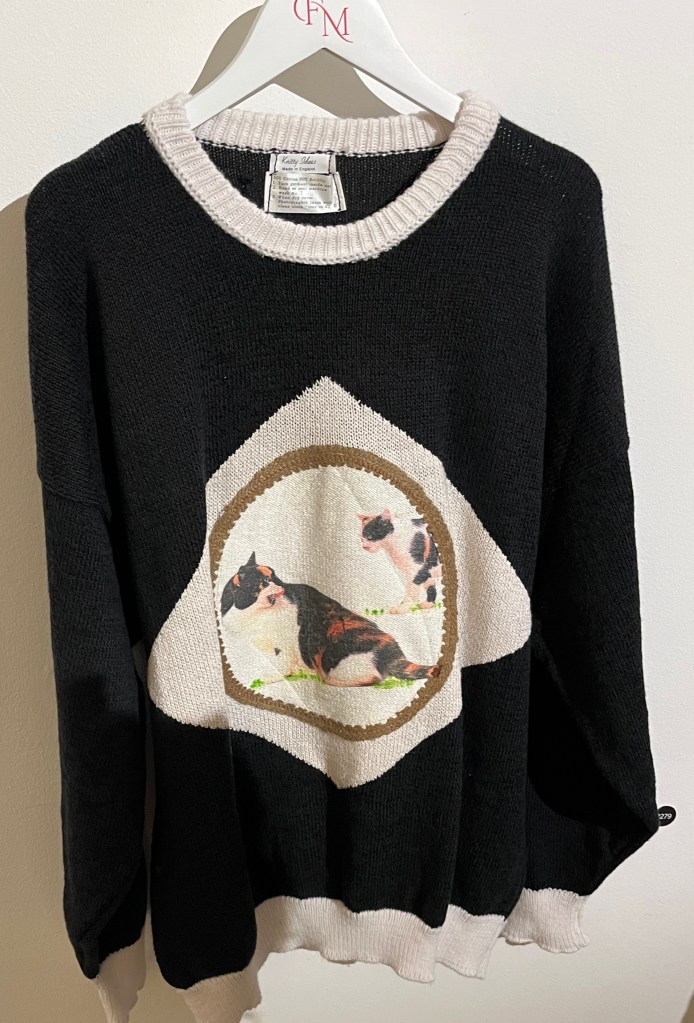A black cotton pullover. The front has a large white diamond shape on it, inside which are colour photographic reproductions of two cats.