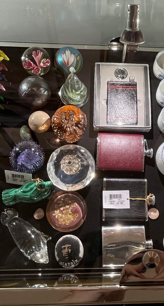 A glass case in the Freddie Mercury exhibition with various items, including paperweights and hip flasks.
