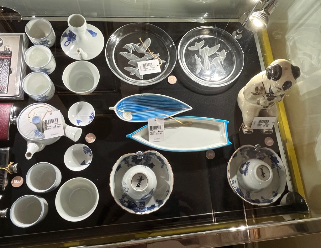 A glass case in the Freddie Mercury exhibition with various items, including Japanese crockery and glass dishes, and a small statue of a Chinese boy.