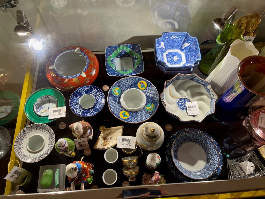 A glass case in the Freddie Mercury exhibition with various items, including Japanese ashtrays, porcelain items and figurines.